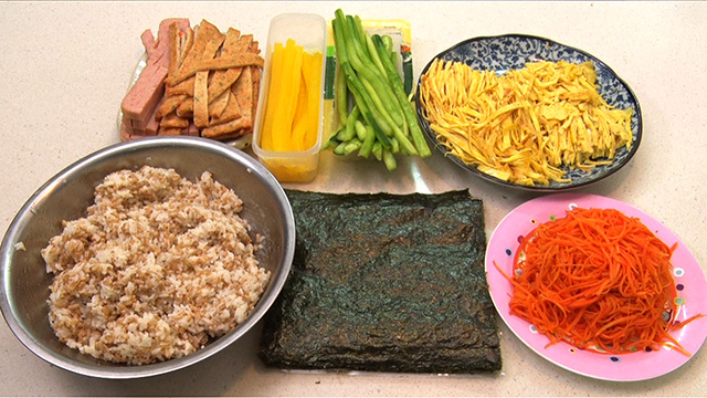 Song-hee fills her kimbap with fish cake, luncheon meat, pickled radish, carrot, cucumber, and strips of fried egg.