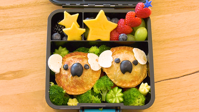 She turns the meat pies into koalas, using tortilla chips for ears, and olives for the nose and eyes. Add some fruit and vegetables, and the koala mom and cub bento is finished.